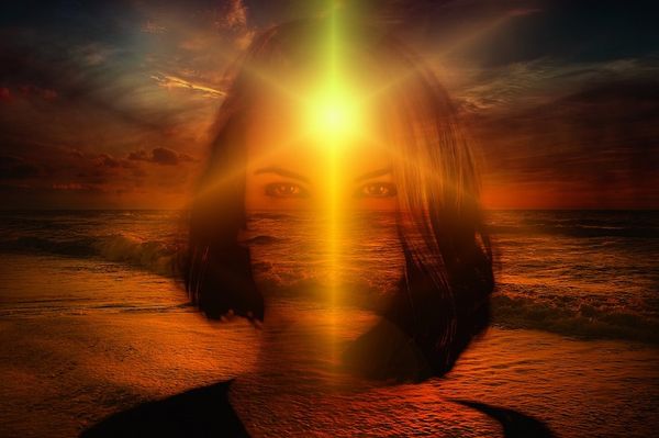 Shadowed fantasy image of a woman looking in the face at sunset on a beach, a sunlight illuminates her face from behind